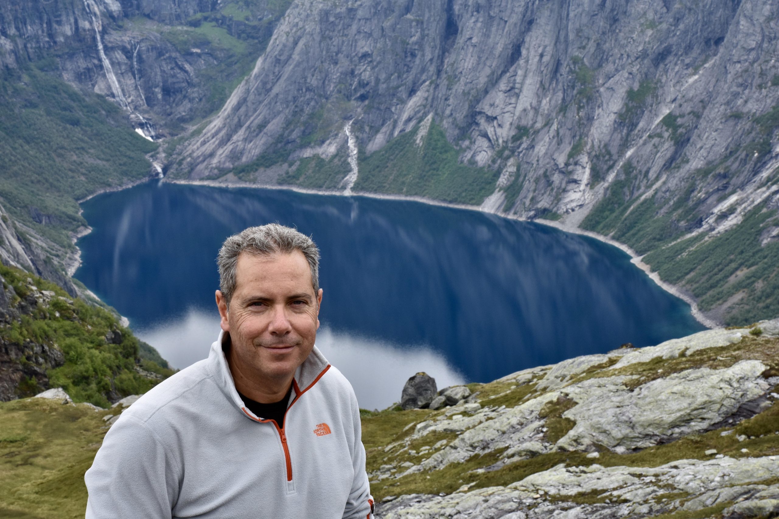 תמונה של בחור ומאחורב יש אגם בין הרים גבוהים