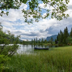 הסירה באגם הפסטוראלי לצד צמחיה ירוקה אינסופית תחת שמים תכולים לבנים - נורבגיה .